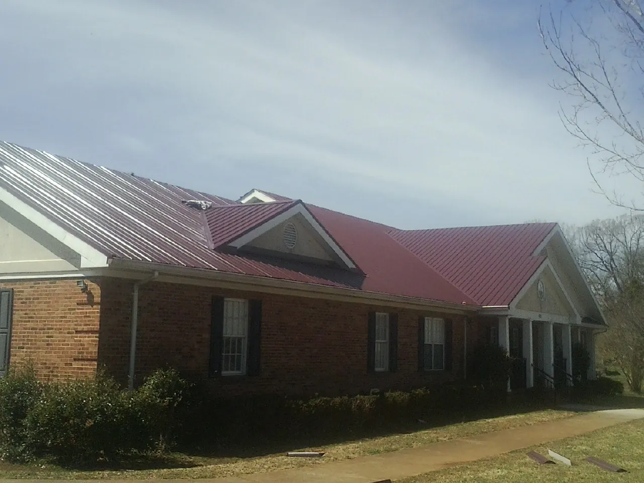Red metal roof with gabled entries on a long brick building, from a Hail Damage Roof Repair job in Barneveld