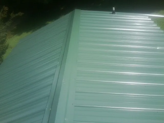 New green metal panels meeting at the ridge of a roof — Flat Roof Repair work by our crew in Barneveld