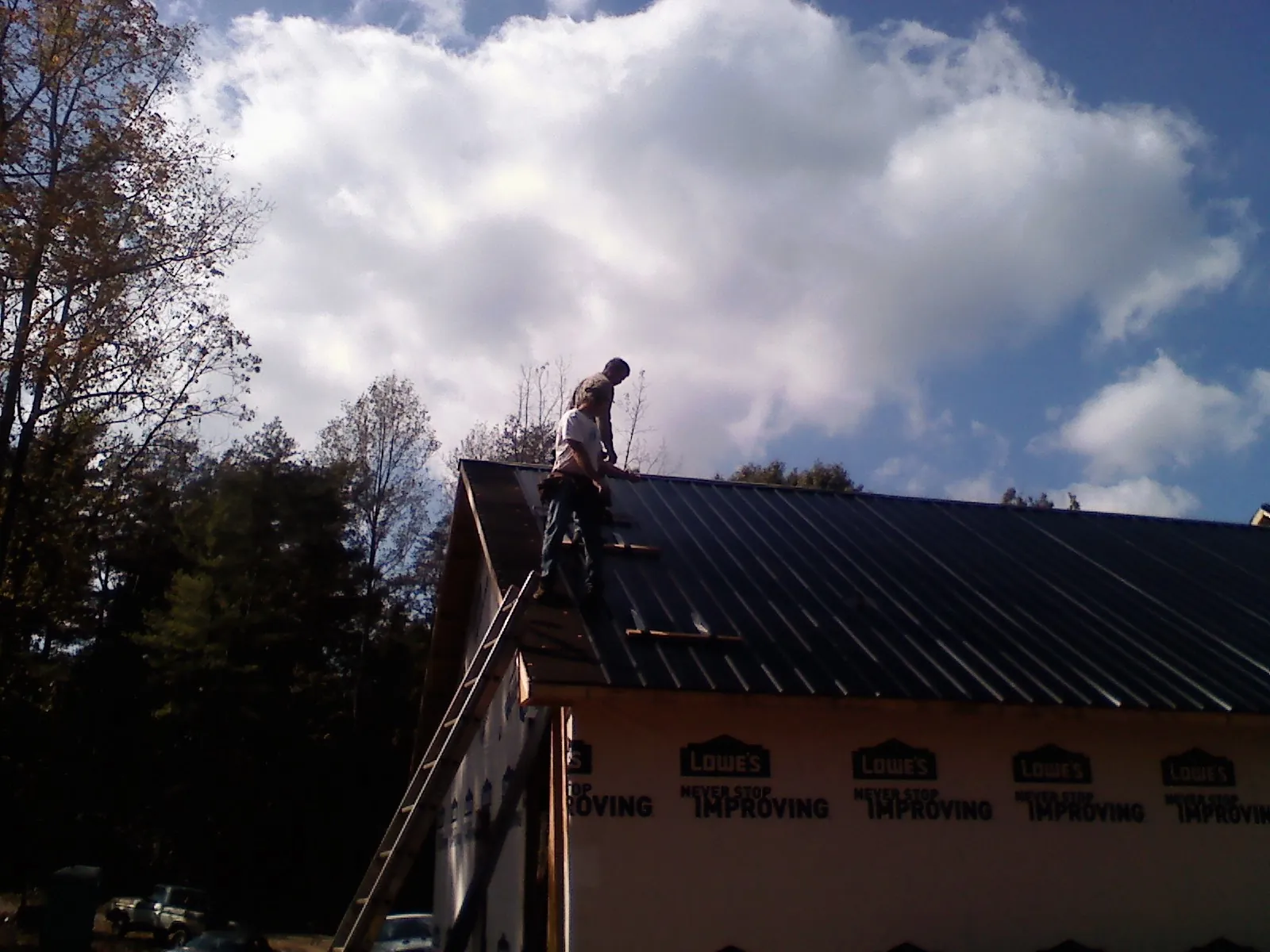 Roofer fastening dark metal panels high against a cloudy sky, from a Roof Inspection job in Barneveld