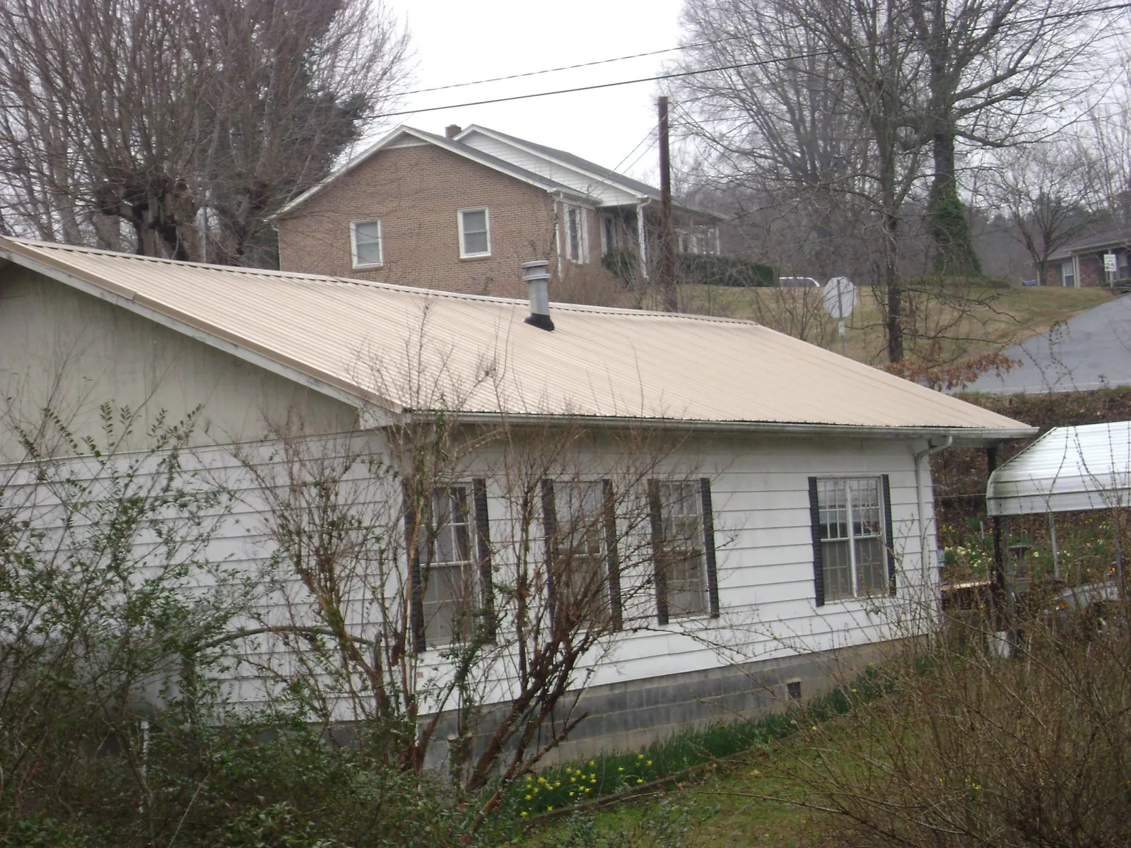 Tan metal roof on a white sided house set into a hillside — Commercial Roofing by Roofing Brothers in Barneveld